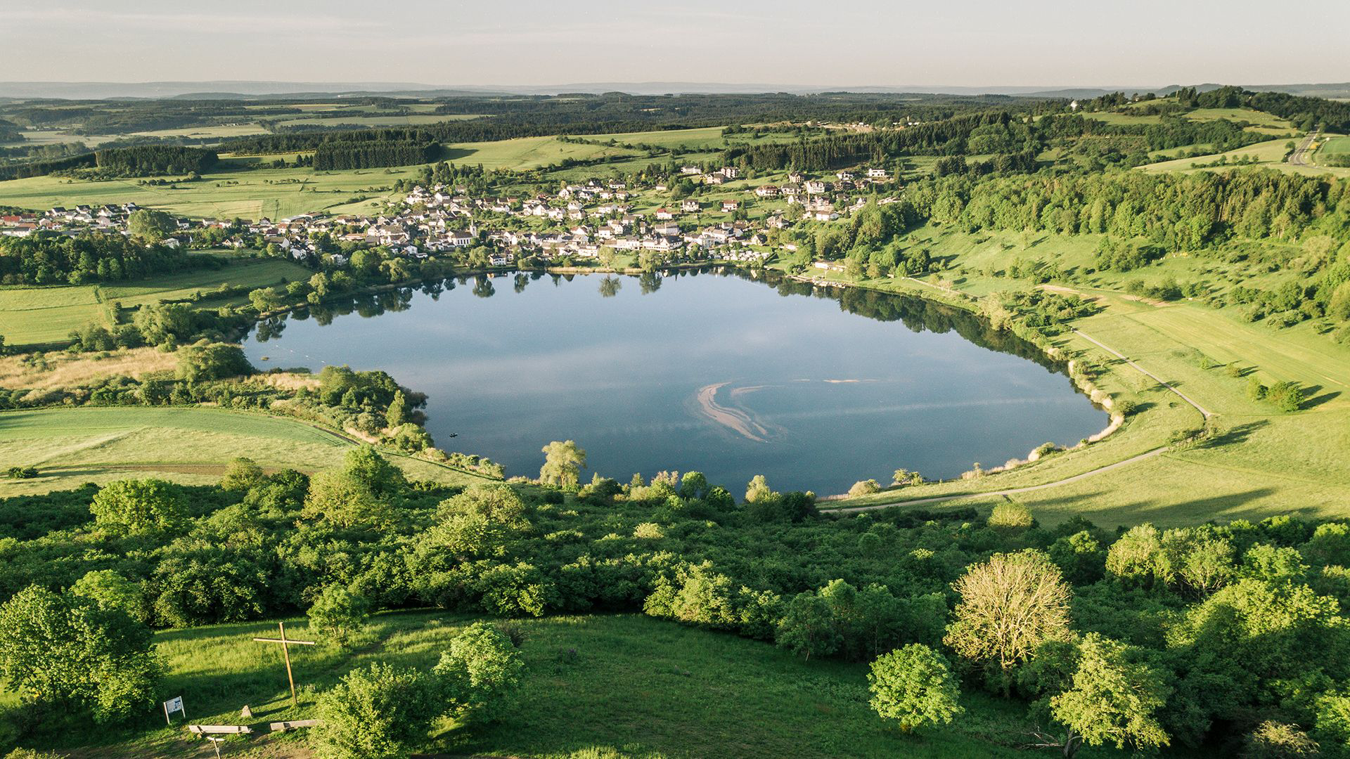 maarsee mit dorf am rand eingebettet in gruene huegel